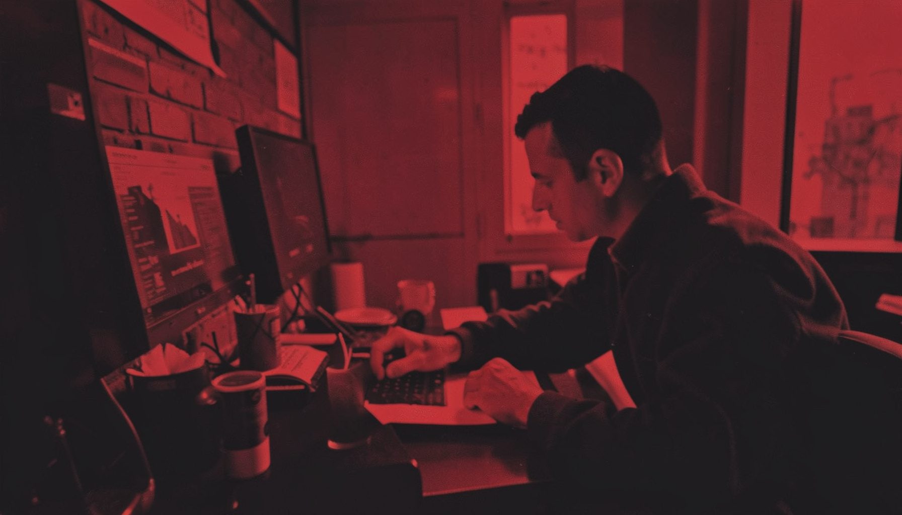Duotone image of a developer at workstation rendered in brick red and dark charcoal tones