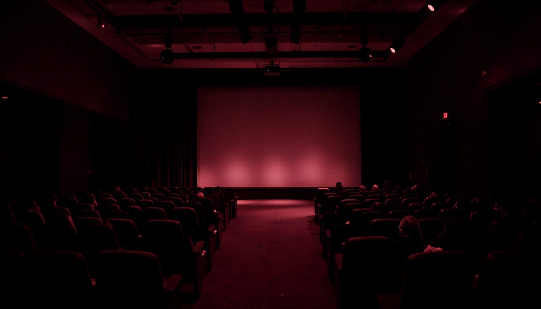 Dark maroon and black duotone photograph of a conference hall with a softly lit stage
